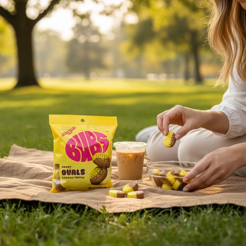 shopnathans.com Bubs Ovals Sweet Banana Toffee candy bag and bowl on a picnic blanket in a sunlit park