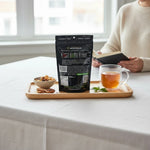 shopnathans.com Pure Infinity Botanicals Green Maeng Da Kratom powder pouch on a wooden tray with tea and a book